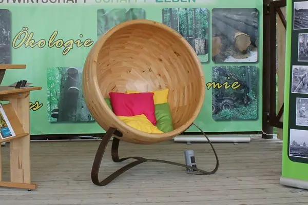 Sitzkugel aus Holz mit bunten Kissen vor einer grünen Informationswand